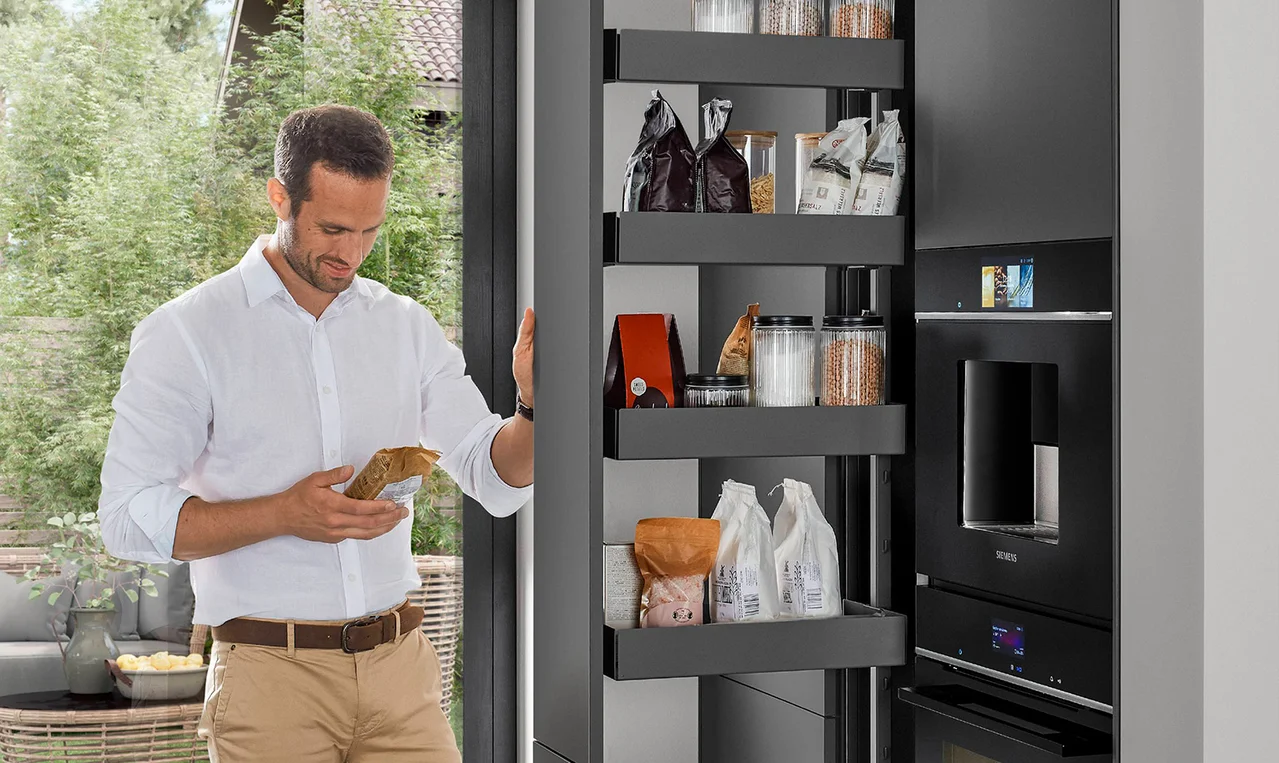 Homme consultant une colonne de rangement optimisée à tablettes coulissantes remplies de provisions Homme consultant une colonne de rangement optimisée à tablettes coulissantes remplies de provisions