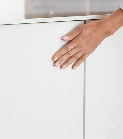 Main effleurant une façade de cuisine blanche ton neutre au design intemporel Main effleurant une façade de cuisine blanche ton neutre au design intemporel
