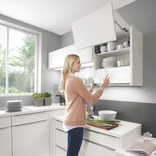 Femme ouvrant un meuble haut à porte relevable dans une cuisine blanche caisson XL Femme ouvrant un meuble haut à porte relevable dans une cuisine blanche caisson XL