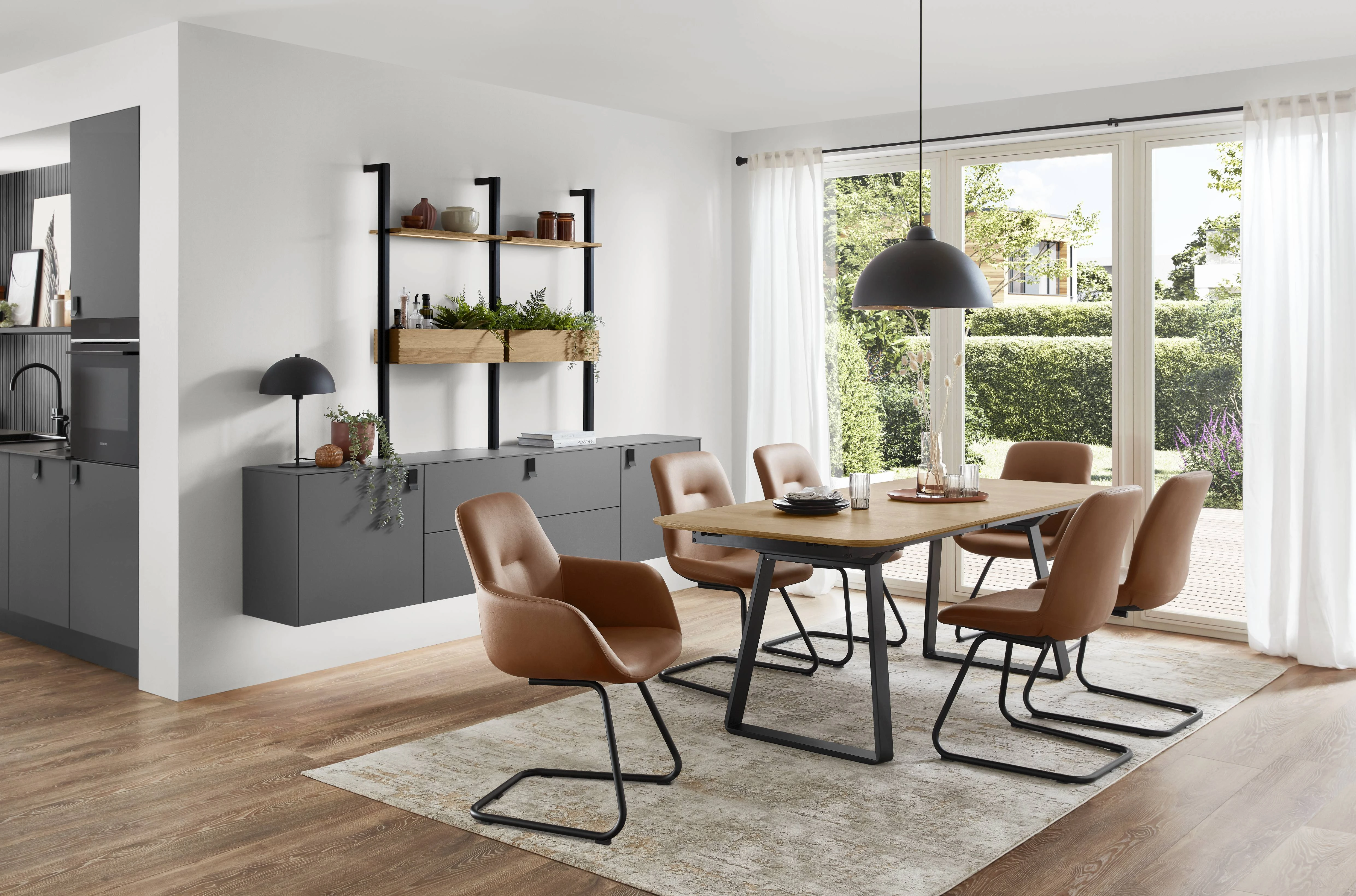 Salle à manger ouverte sur cuisine avec table en bois, chaises en cuir camel et suspension noire Salle à manger ouverte sur cuisine avec table en bois, chaises en cuir camel et suspension noire